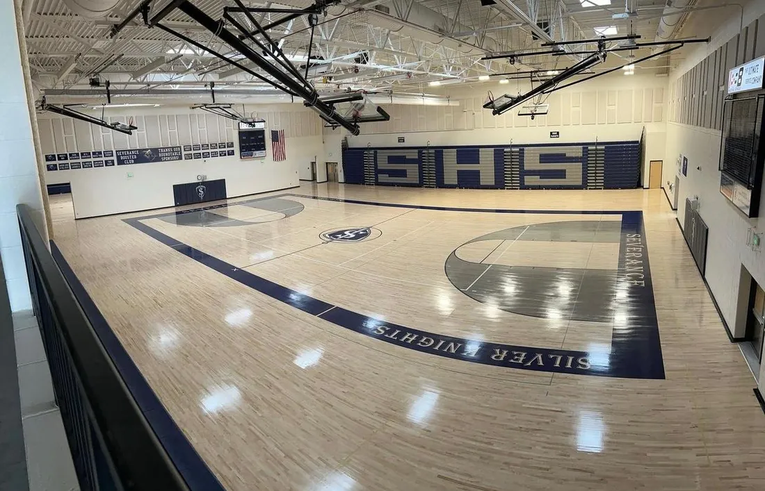 Finished maple gymnasium floor with painted lines and a school logo at center court
