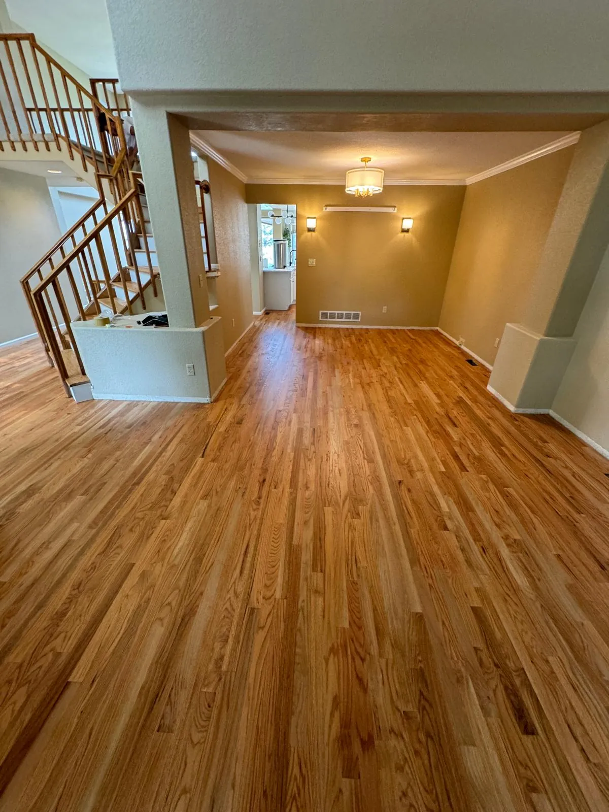 Red oak floor refinished through an open living and dining room, staircase in the background