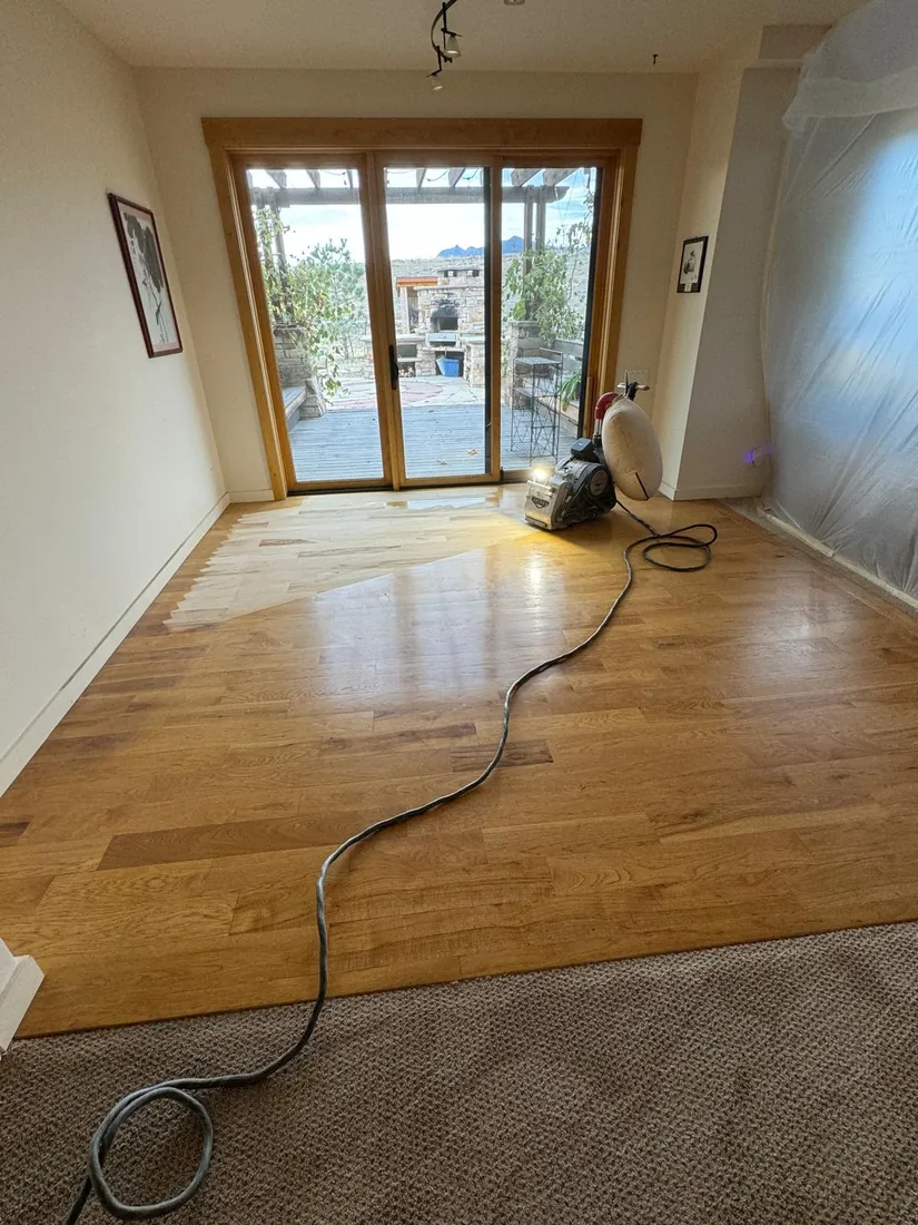 A floor sander at work taking a hardwood floor back to bare wood beside a kitchen island