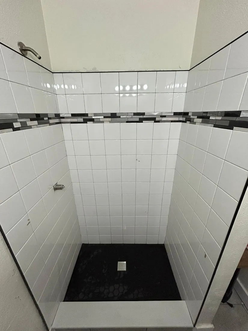 Finished shower in white tile with a mosaic accent band and dark stone base